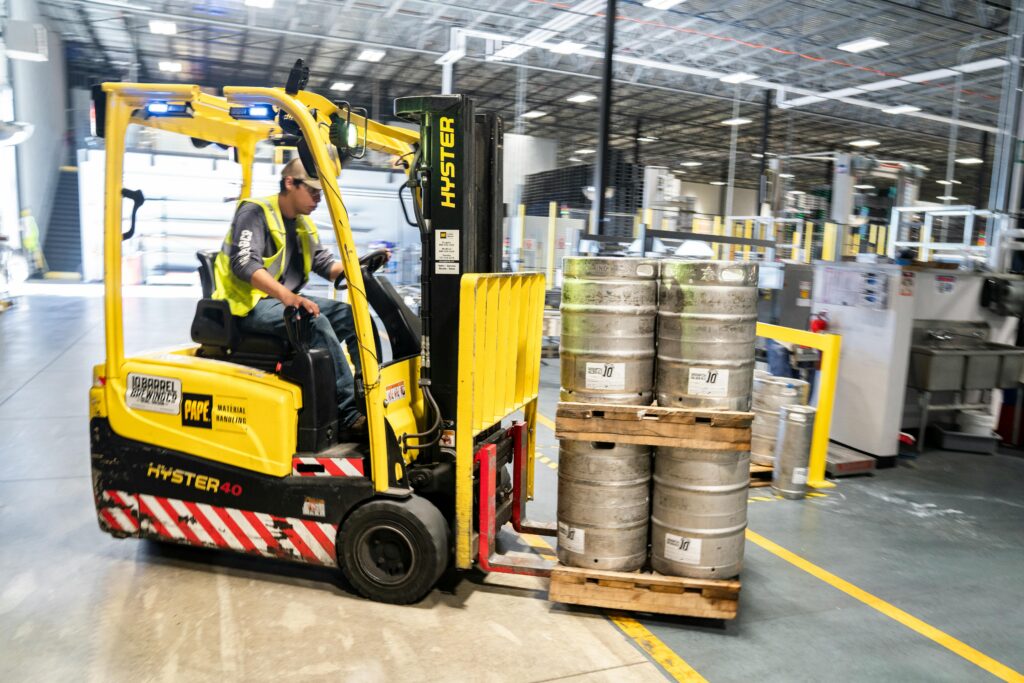 pexels-photo-1267337-1267337 Forklift operator in warehouse moving beer kegs for distribution.